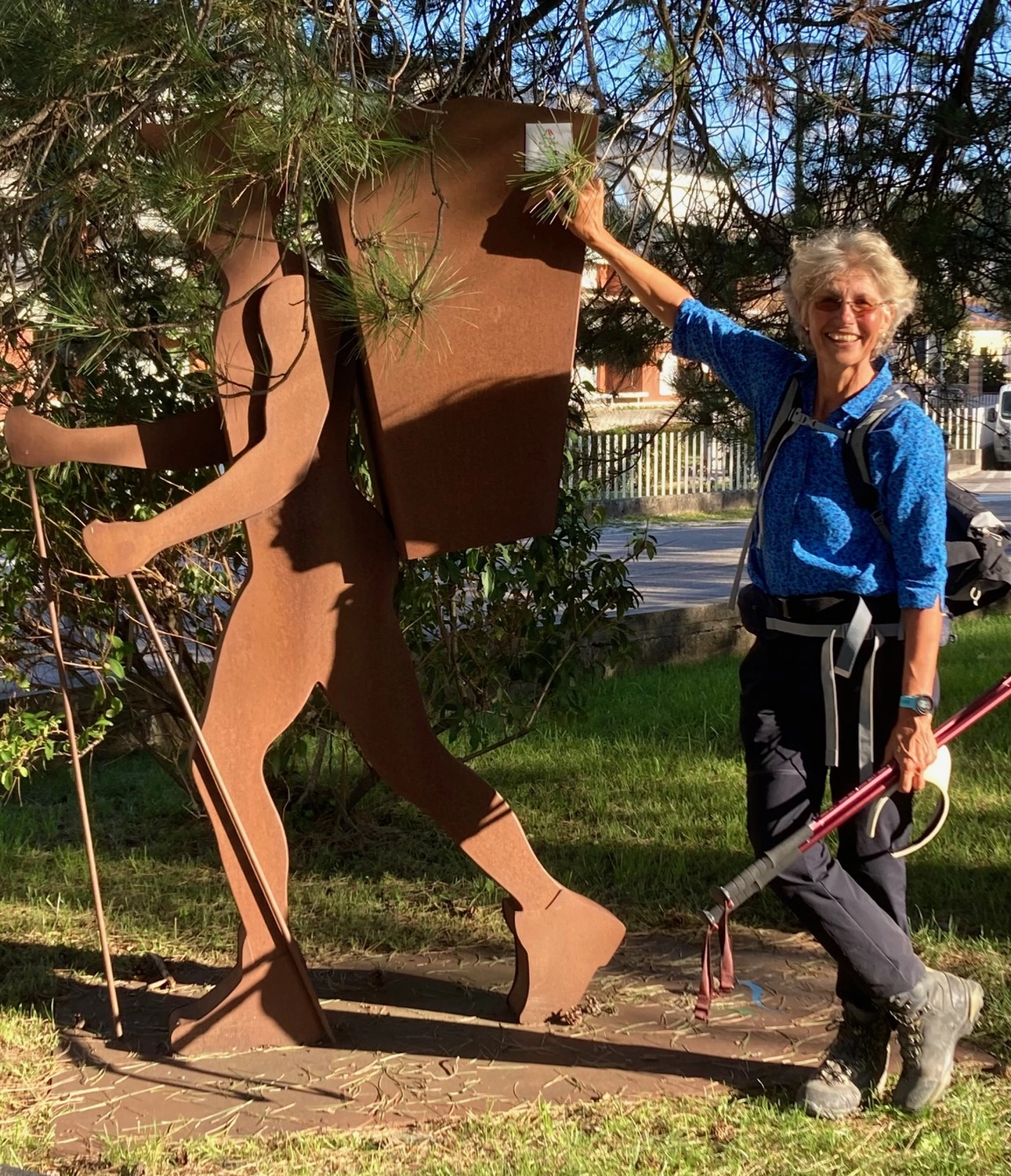 Mindtrail - Coaching und Mentoring - Eine Person in einem blauen Hemd lächelt und steht neben einer großen, abstrakten, rostigen Metallskulptur in einer Gartenanlage.