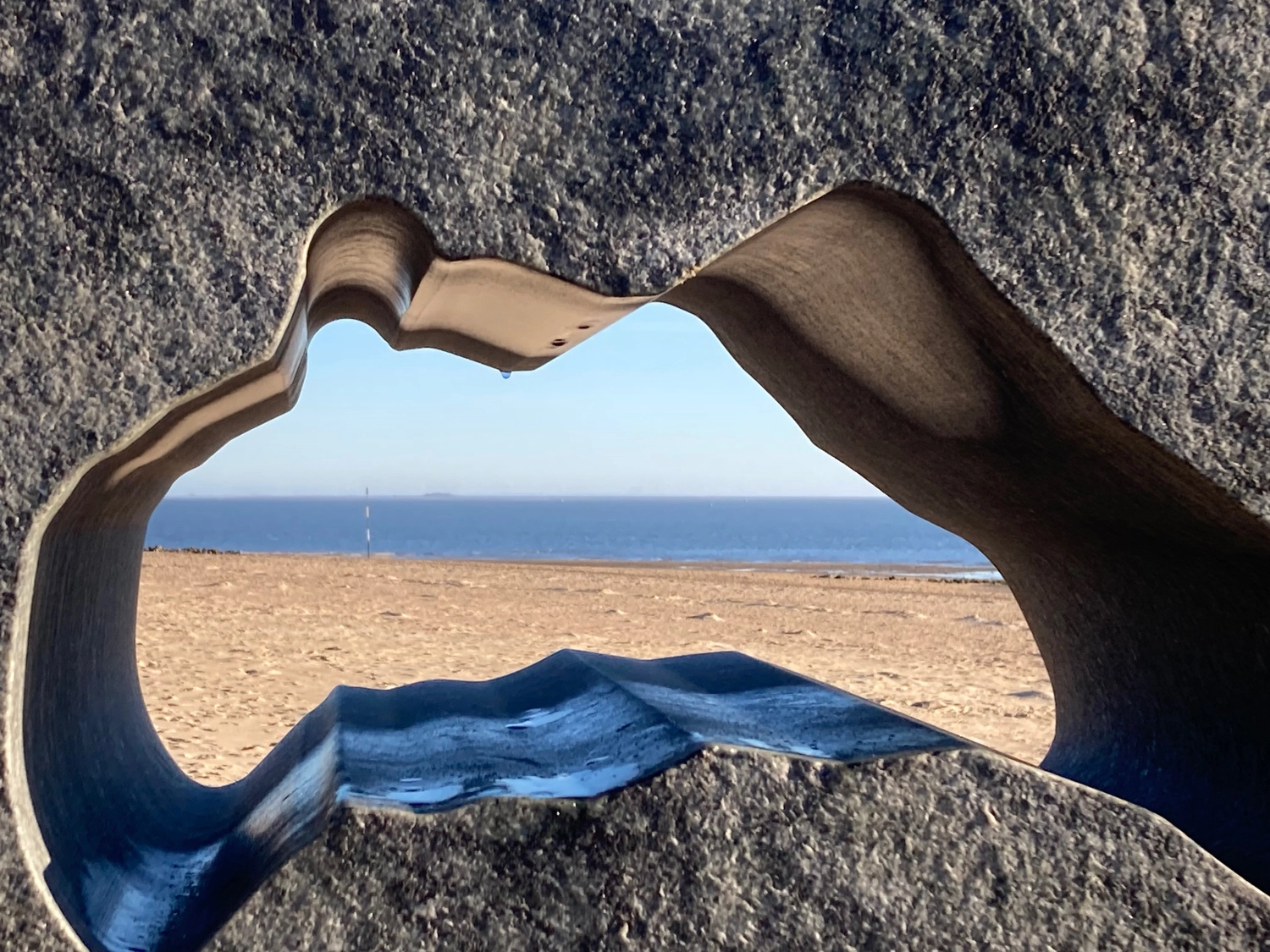 Mindtrail - Coaching und Mentoring - Eine große Felsformation an einem Strand, die auf natürliche Weise den Blick auf Meer und Himmel einrahmt.
